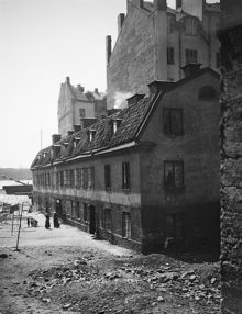 Gårdssidan söderut vid Garvargatan 9. Några kvinnor och barn står på gården där tvätten hänger på tork, tvättlinorna är fästade i husväggen