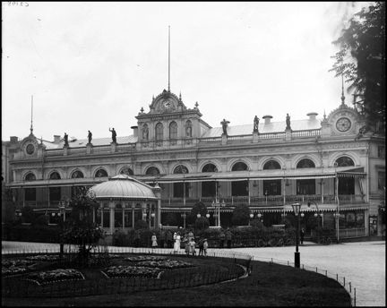 Berns salonger. En plantering och en samling människor syns framför byggnaden.