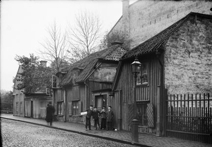Styrmansgatan 32 och 34 norrut mot Storgatan. Utanför porten till Styrmansgatan 32 står en grupp pojkar och vid fönstret en trappa upp sitter en skvallerspegel.