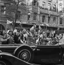 Fredsdagen den 7:e maj 1945. 

Glada människor i bilar och på gatan viftar med flaggor på Birger Jarlsgatan.