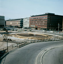 Vy från Malmskillnadsgatan mot varuhusen Åhlens och EPA. Fontänen vid Sergels Torg under uppbyggnad med armeringsjärn och gjutformar