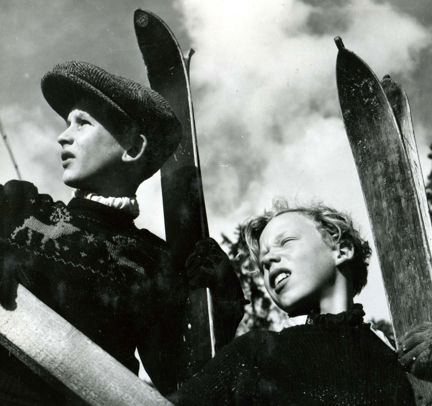Två barn tittar åt sidan och håller i varsitt par skidor