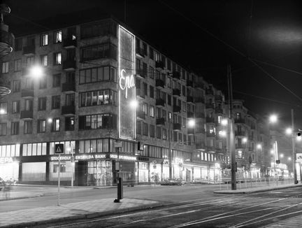 Skyltfönster och ljusreklam på fasad i mörker.