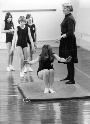 Flickor gör kullerbyttor i gymnastiksal