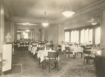 Dukade bord med vita dukar. Längs ena långsidan fönster, i taket ljusarmaturer.