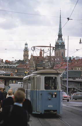 Spårvagnen kommer fram till personer som står och väntar. Gamla stans bebyggelse, med Tyska kyrkan och Storkyrkan, i bakgrunden.