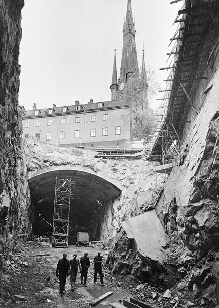 Tunnelbanan byggs. Vy från Vasagatan 22 österut genom rivna kv. Kajan, nu Orgelpipan 6. I fonden ligger Klara Västra Kyrkogata 20 och Klara kyrkas torn