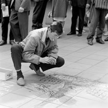 Gatukonstnär i arbete med en målning på trottoaren