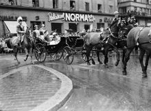 Sveavägen 23, kunglig kortege. Kung Gustaf V fyller 85 år och rider kortege genom staden. I vagnen sitter även kronprinsessan Louise och kronprinsen Gustaf Adolf. I bakgrunden t.h. Restaurant Norma