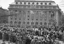 Gustav Adolfs Torg, mot kvarteret Vinstocken - Skandinaviska Banken. Folksamling ser på Norges kung Haakon och Gustaf VI Adolf i kortege genom Stockholm under kung Haakons officiella besök