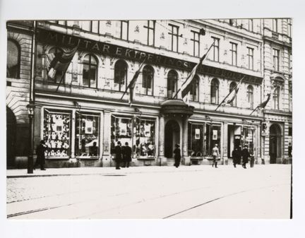 Svartvit bild av en exteriör med människor på gatan utanför. 