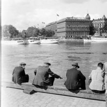 Några män sitter på kajkanten vid Skeppsbron