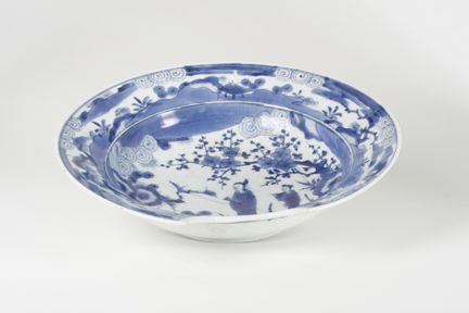 Ett fat fotograferat aningen uppifrån, mönstrat i blått och vitt med ett motiv föreställande två japanska kvinnor, körsbärsblom och ett landskap.