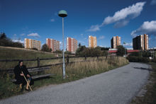Kvinna på parkbänk, i bakgrunden höghusen i Akalla.