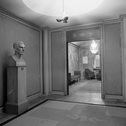 Bystskultur på en sockel. En dörröppning mot ett rum med sittmöbler.