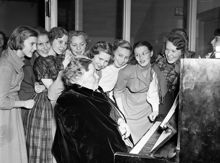 Timmermansgatan 21. Julfest på Södermalms kommunala flickskola. Ungdomar och en äldre dam samlade runt ett piano