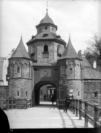 Träbro som leder in igenom stadsport, en människa står lutad mot räcket