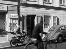 Holmströms Skor vid Mäster Samuelsgatan 42 och Alma Björks Bosättningsmagasin vid Mäster Samuelsgatan 40. En man passerar österut på cykel. Här går numera Sveavägen norr om Sergels Torg