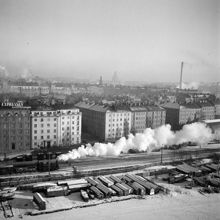 Ett ånglok på järnvägsspåret vid Atlasmuren. Båtskjul vid Barnhusviken. Husen i fonden ligger vid Atlasmuren 18-6