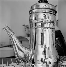 Självporträtt speglat i rostfri kaffekanna. Fotografen befinner sig i en köksinteriör