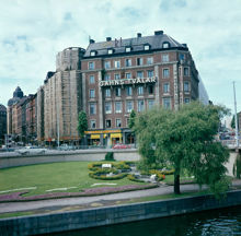 Kungsbroplan; liten park med blomformad plantering. Vy mot kv. Härolden, Kungsg. och Fleminggatan. I fonden bl.a. dansrestaurangen Kungsbrohof-