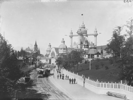 Människor promenerar bredvid staket, i bakgrunden syns torn