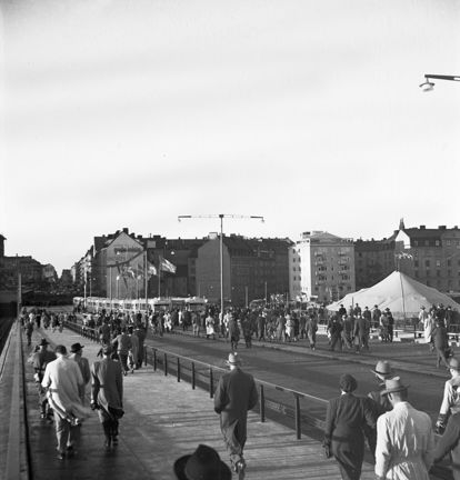Vy bakifrån över en mängd personer som korsar bron. I bakgrunden står några spårvagnar på bron.