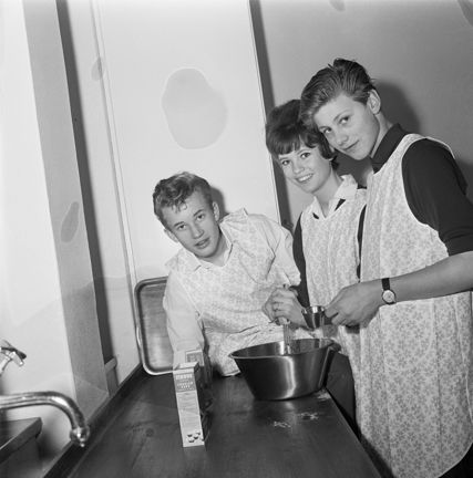 En kvinna och två pojkar med förkläden står i ett kök och bakar.