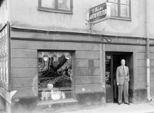 Beridarbansgatan 27. Sten Rocke Antikvitets AB. En grävmaskinsskopa avspeglas i skyltfönstret