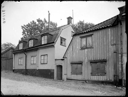 Bebyggelse, främst i trä, längs gatan. Intill husen övergår gatan i gräs.