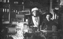 Interiör från Livsmedelsaffär på Götgatan 77 omkring år 1915. På bilden syns fru Augusta Norgren tillsamman med sonen Harry.