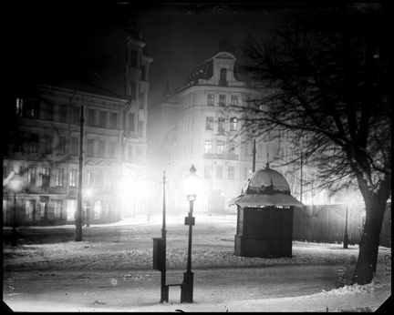Lyktor lyser starkt upp i mörkret. I bakgrunden står en kiosk med snö på taket.