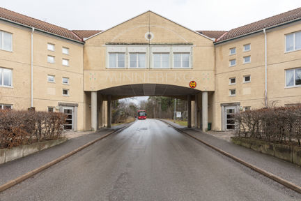 En putsad fasad med väg under en portal i Minneberg.  I bakgrunden syns en buss.