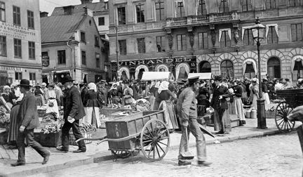 Trångt med människor på torget. En handdragen kärra i förgrunden.
