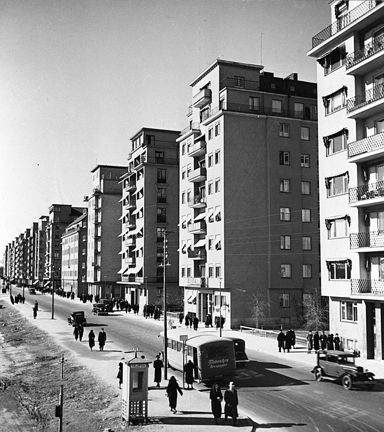 Norr Mälarstrand sedd västerut. De höga flerbostadshusen vänder kortsidorna mot gatan, där det finns bussar, bilar och promenerande människor. 