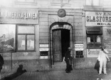 En man passerar porten till Skeppsbron 18. Fasaden och fönstren har skyltar för olika företag bland annat ""Amerika-Linien""