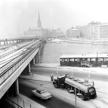 Vy från Slussen längs tunnelbanebron mot Mälartorget och Riddarholmen. I förgrunden tankbil vid bensinpumpar på Sjöbergsplan samt byggbaracker