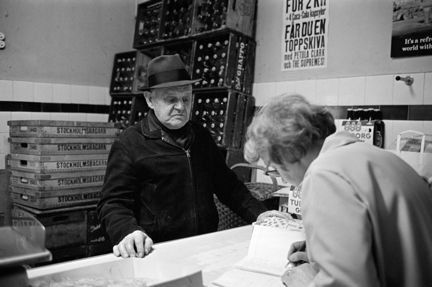 Norra Smedjegatan 5. Man som handlar i Maja Erikssons mjölkbutik. Maja Eriksson skriver in summan i sin kassabok.