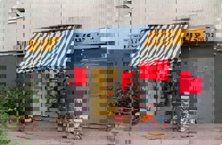 En man står utanför en livsbutik med randig markis och handskrivna anslag utanför.