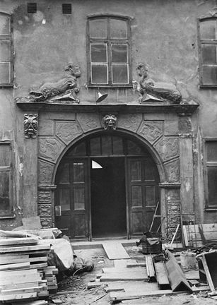 en portal i sten med utsmyckning av fiskar. framför portalen ligger byggnadsmaterial.