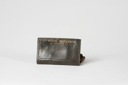 Plånbok fotograferad från baksidan. En text i guld i överkant lyder: CAPT. PETER BECKSTRÖM FRA STOCKHOLM 1783. Namnet är större än övrig text. Plånboken är naturligt sliten.