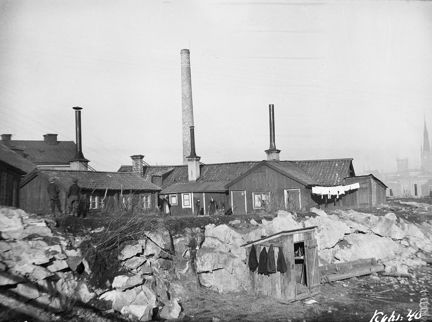 Svartvitt foto över låga trähus och skorstenar 