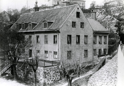 En svartvit bild av ett äldre hus som tidigare var Södra varvets bostad för varvschefen. Träd och trappor finns runtom huset och ett hus bakom.