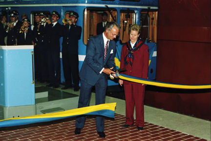 Kung Carl XVI Gustaf klipper ett blågult band på en tunnelbaneperrong. Ett tunnelbanetåg och en blåsorkester i bakgrunden.