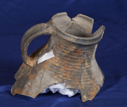 Övre delen av en medeltida kanna av svartgods. Fotograferad mot blå bakgrund. 