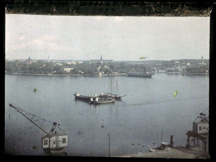 Lyftkranar synd på Stadsgårdskajen, ute på vattnet ligger några båtar i en klunga och på andra sidan skymtar bland annat Nordiska museet.