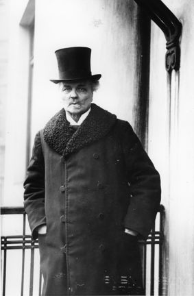 August Strindberg står på sin balkong i vinterrock och hög hatt