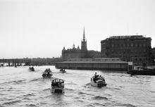 Riddarfjärden. Småbåtars hemkomst från söndagstur. T.v. Centralbron och tunnelbanebron under uppbyggnad. Riddarholmskyrkan i fonden. T.h. flytande fiskhall vid Kornhamnstorg och Cederlundska huset
