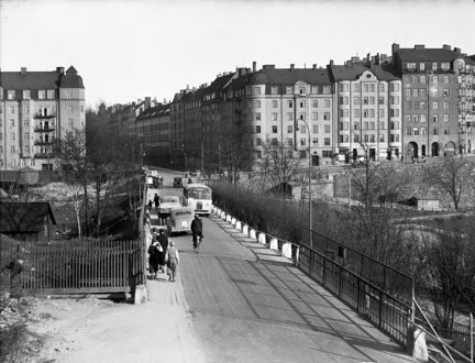 Cyklister, bilar och gångtrafikanter på Tomtebodabron. I bakgrunden flerbostadshus.
