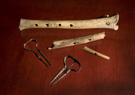 Två medeltida mungigor och tre benflöjter av olika storlekar. Fotograferad mot röd bakgrund. 